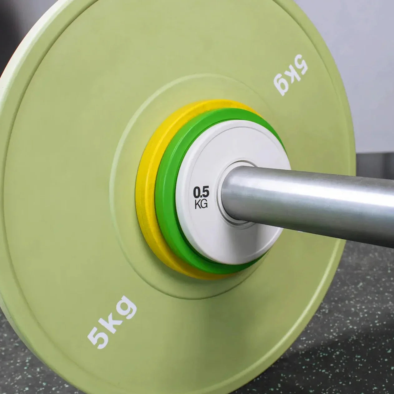 Close-up of a green weight plate with a silver barbell on a dark surface